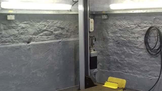 Workshop interior with a yellow platform lift, stone walls, and overhead lighting.