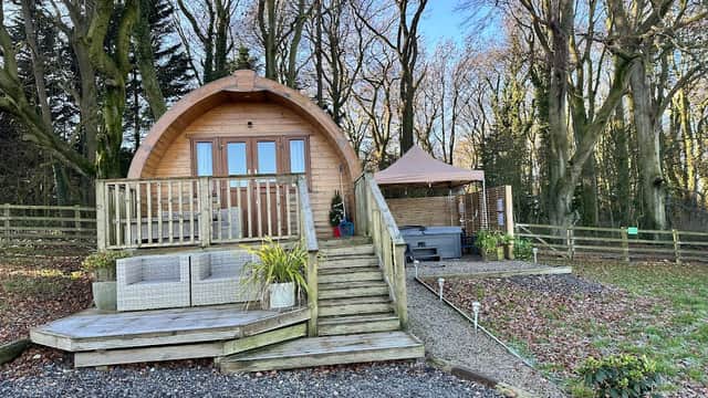 Wooden cabin with a deck, surrounded by trees, steps leading up, and a gazebo nearby in a tranquil setting.