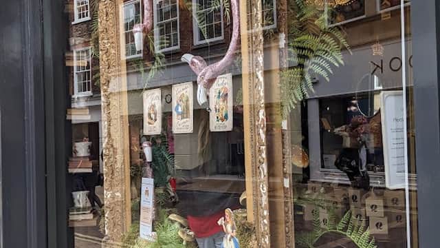 Charming shop window featuring ornate mirrors, decorative items, ferns, and a vintage clock in a quaint York street.