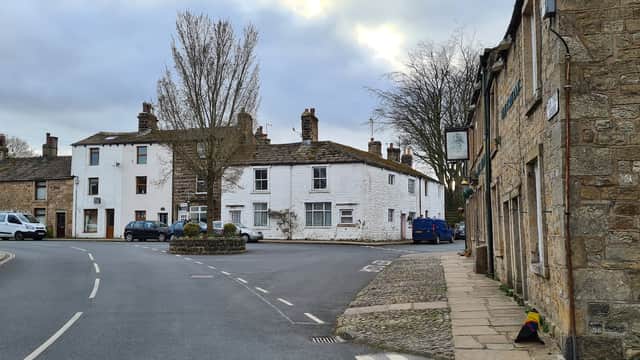 Main St Car Park in Skipton, featuring stone buildings, a roundabout, and parked cars under a cloudy sky.