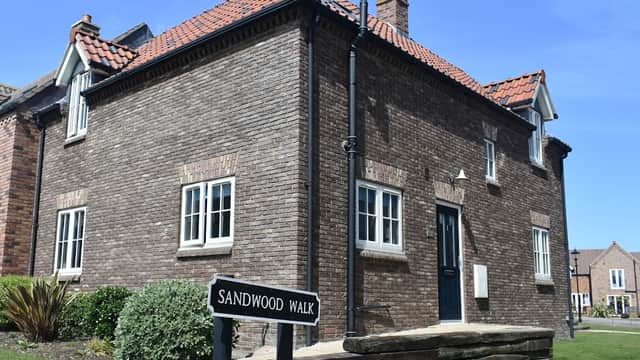 A brick house with a dark door and white windows, surrounded by green grass and a sign for Sandwood Walk.