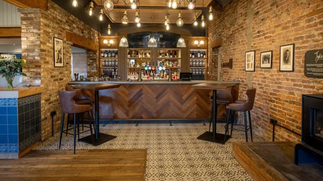 Stylish bar area with wooden flooring, exposed brick walls, and pendant lights, featuring high stools and a patterned tile floor.