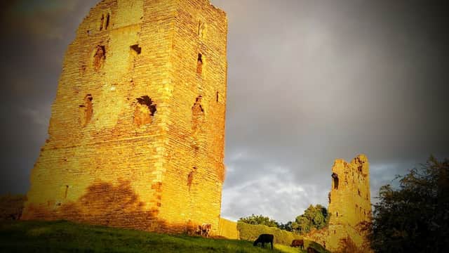 Historic stone ruins on a grassy hill, with grazing cows and a dramatic sky in Sheriff Hutton, Yorkshire.