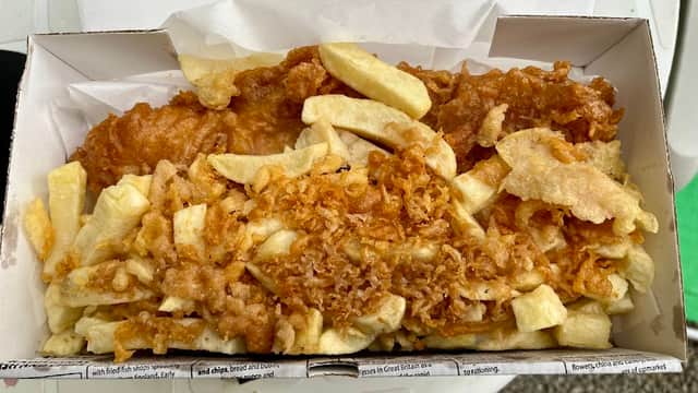A takeaway box filled with golden-brown battered fish and crispy chips, resting on a white surface.