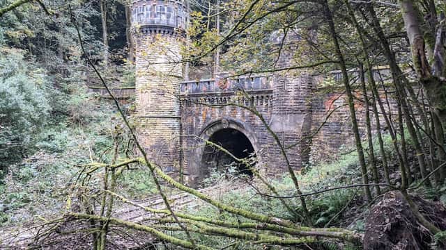 North portal of Bramhope Tunnel, featuring a stone archway and a tower, surrounded by lush greenery and fallen branches.