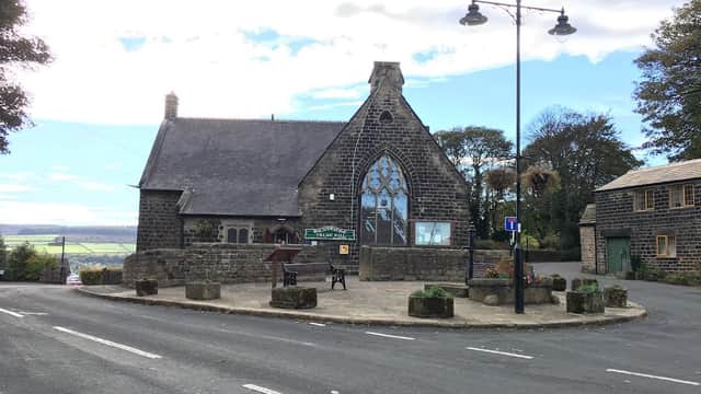 Bolsterstone Village Hall with a large stained glass window, surrounded by greenery and a circular stone seating area.