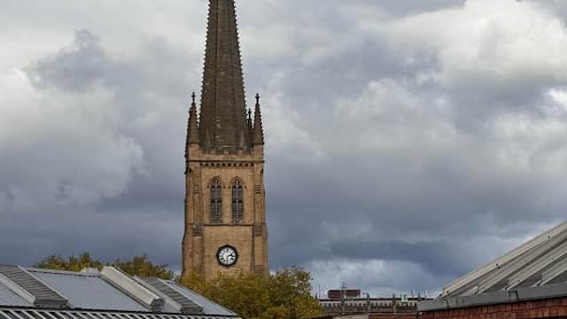 Car park at The Ridings Shopping Centre with cars and a church steeple in the background under a cloudy sky.