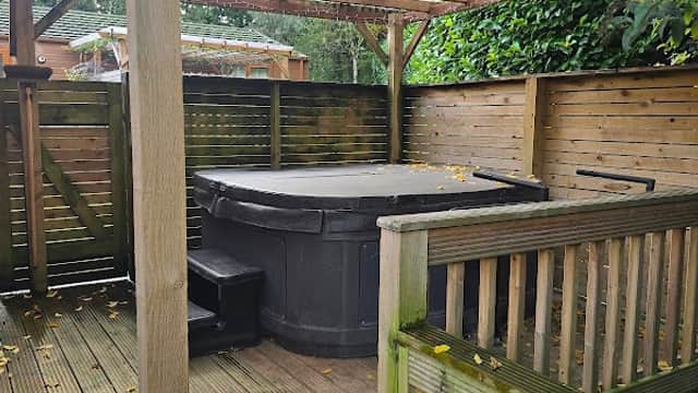 Hot tub under a wooden pergola, surrounded by wooden fencing and greenery at Croft Park Holiday Lodges.