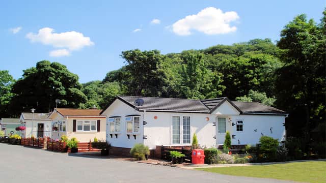 Caravans lined along a paved path, surrounded by trees and blue sky with fluffy clouds in Richmond Caravan Park.