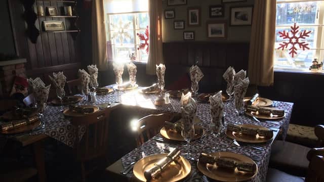 Tables set for a festive meal with gold plates, folded napkins, and Christmas decorations in a cozy pub interior.