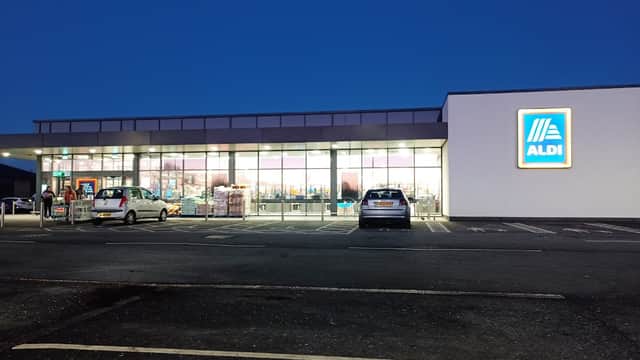 ALDI store exterior at dusk, featuring large windows and a prominent logo, with parked cars in the foreground.