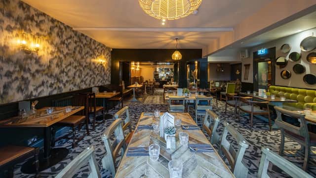 Stylish bar interior with wooden tables, green seating, patterned carpet, and decorative lighting.