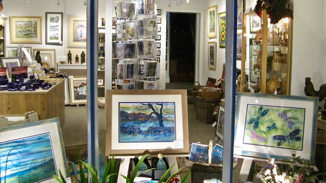 Art gallery display featuring framed artworks, sculptures, and various art supplies in a well-lit space.