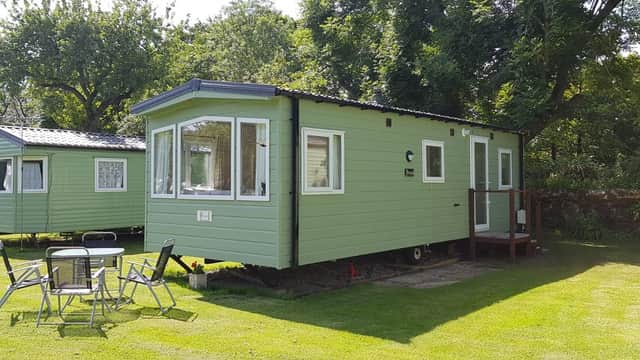 Green caravan with large windows, surrounded by grass and trees, at Orchard Caravan & Camping Park in Reeth, Yorkshire.