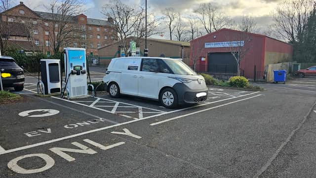 Electric vehicle charging station with a parked van in a car park, surrounded by trees and buildings.