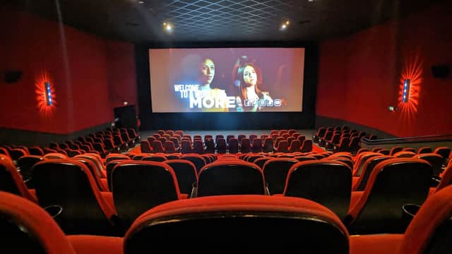 Interior of a cinema with red seating and a large screen displaying a film, creating a cozy atmosphere.