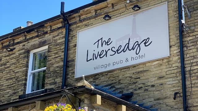 Sign for "The Liversedge" pub and hotel on a stone building, with a hanging flower basket and clear blue sky.
