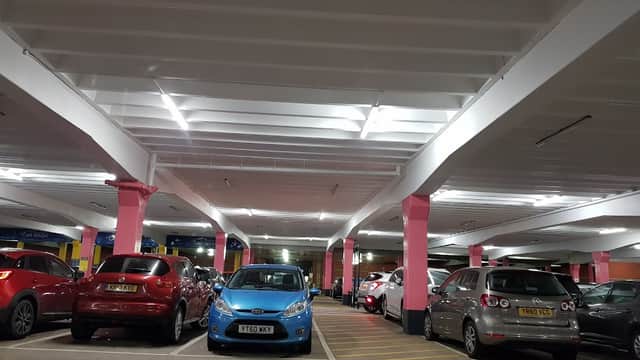 Brightly lit car park with pink columns, featuring various parked cars including a blue one.