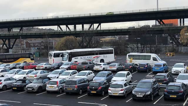 Meadowhall staff car park filled with cars and buses, under a railway bridge, cloudy sky overhead.