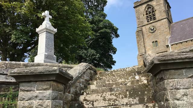 Stone steps lead to a church tower with a clock, surrounded by trees under a clear blue sky.