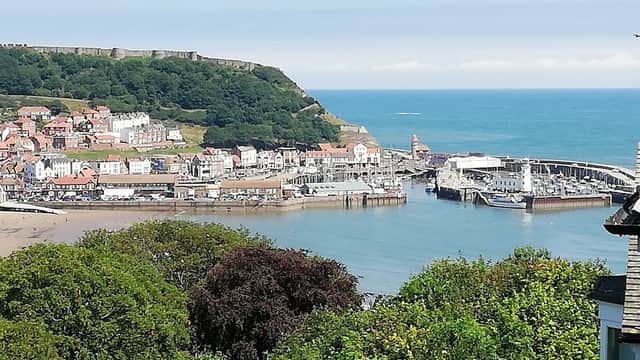 View of Whitby harbor with colorful buildings, boats, and lush green hills under a clear blue sky.
