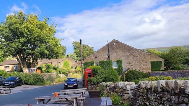 Quaint hotel with stone buildings, picnic tables, a red telephone box, and lush greenery under a blue sky.