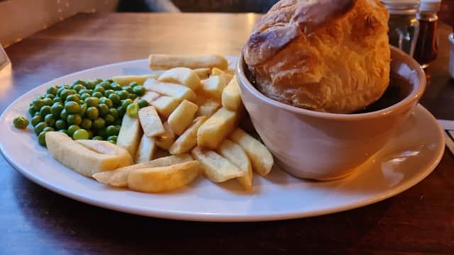 A plate with chips, green peas, and a large pie on a wooden table.