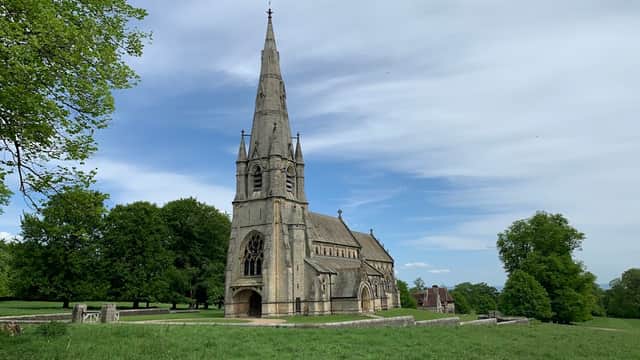 Gothic-style church with a tall spire surrounded by lush greenery and blue sky at Studley Royal Deer Park.