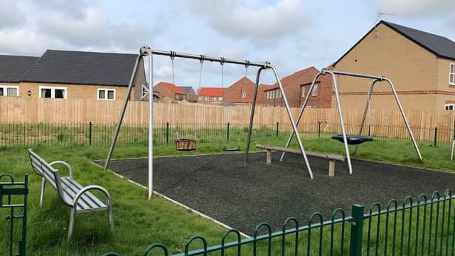 Play area with swings and a bench, surrounded by grass and residential houses in Great Driffield, Yorkshire.