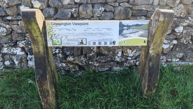 Signpost for Grassington Viewpoint, featuring a map and information, set against a stone wall and grassy area.