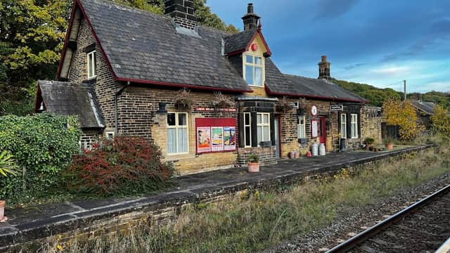 Historic railway station building with stone walls, slate roof, and surrounding greenery, set against a dramatic sky.