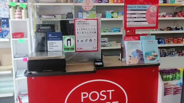Post office counter with red signage, medicine shelves, and promotional displays in a bright, organized space.