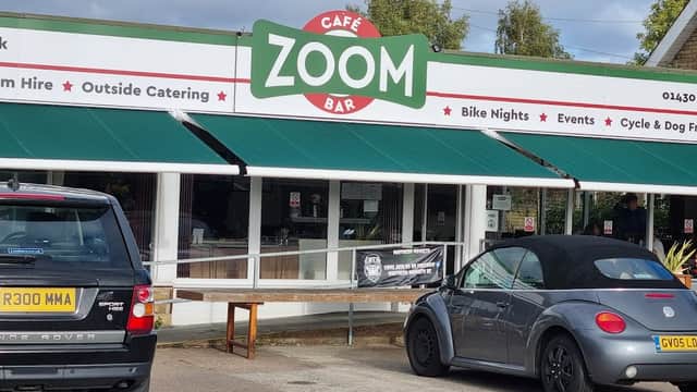 Zoom Cafe Bar features a green awning, outdoor seating, and parked cars in front of a welcoming storefront.