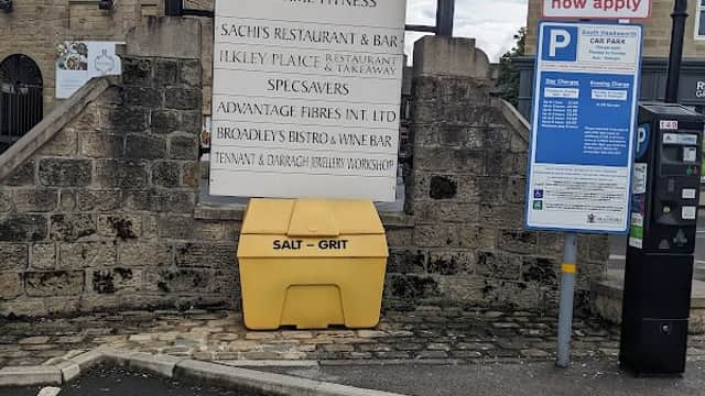 Signage for local businesses and parking information, with a yellow salt grit bin in the foreground.