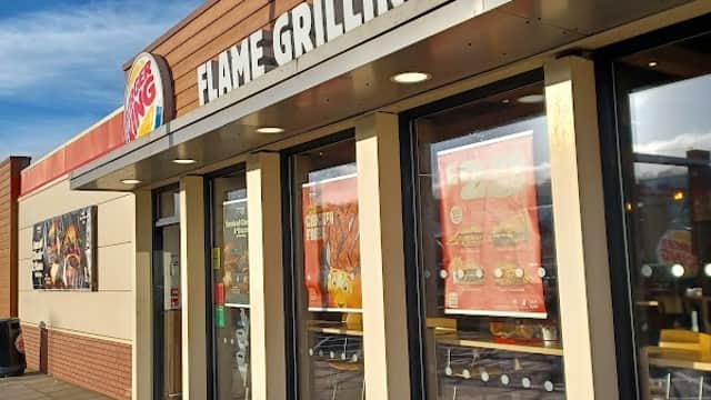 Burger King storefront with large windows, showcasing the sign "FLAME GRILLING SINCE" against a blue sky.