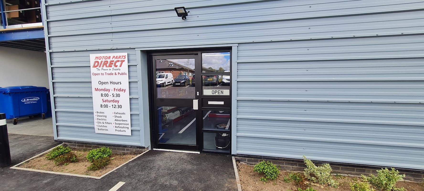 Entrance to Motor Parts Direct with an "OPEN" sign and operating hours displayed on the wall.