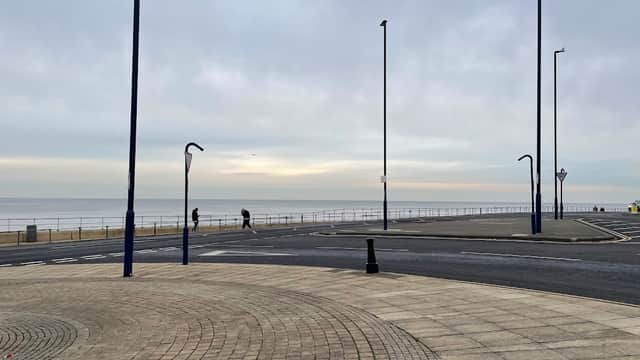 View of Redcar High Street East, featuring a wide promenade, streetlamps, and a calm sea under a cloudy sky.