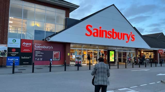 Sainsbury's storefront at Monks Cross Shopping Park, with various store signs and a shopper approaching.