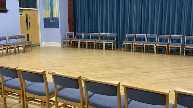 Interior of Wibsey Methodist Church featuring wooden chairs arranged in a circle on a wooden floor with blue curtains.