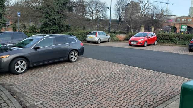 Maude Street Parking Area in Leeds, featuring parked cars and a paved surface, with trees and buildings in the background.
