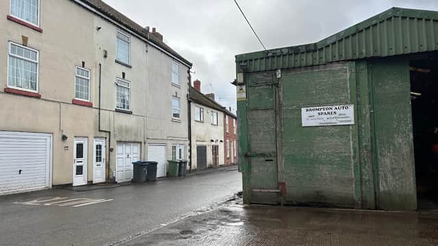 Brompton Auto Spares sign on a green building beside residential houses and parked bins on a wet street.