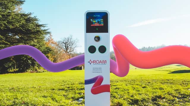 Charging station with a digital display, set in a green landscape with colorful abstract shapes around it.