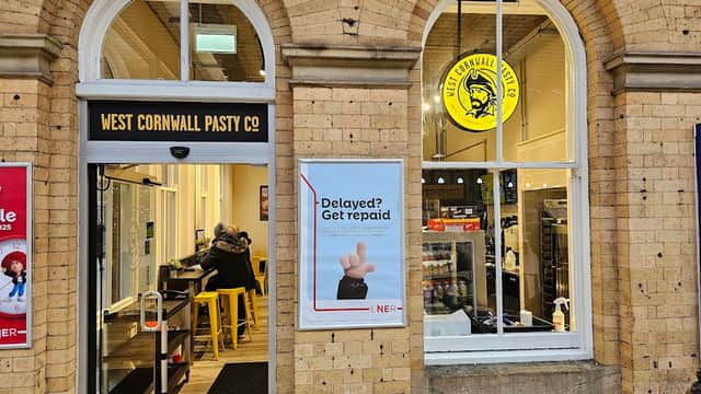 West Cornwall Pasty shop entrance with large windows, yellow signage, and a poster about delays. Customers inside.