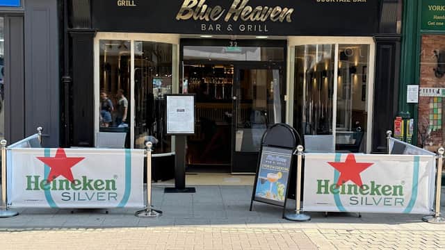 Entrance to Blue Heaven Bar & Grill featuring outdoor seating, Heineken banners, and a menu display.