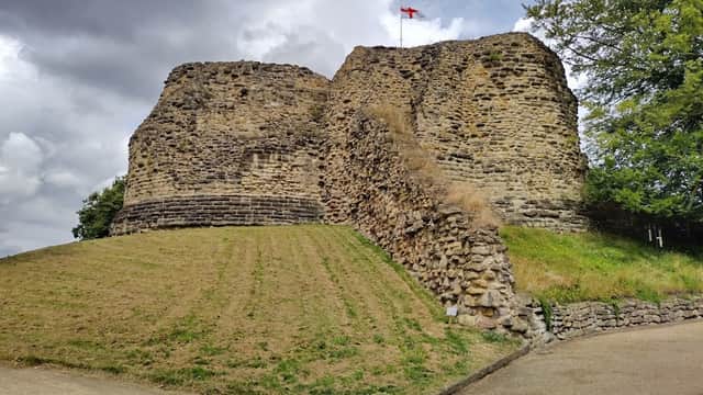 Pontefract Castle ruins with grassy slopes and a flag atop, under a cloudy sky in Yorkshire. Free parking nearby.