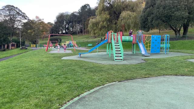 Colorful playground equipment with slides and climbing structures in a grassy park setting. Trees in the background.