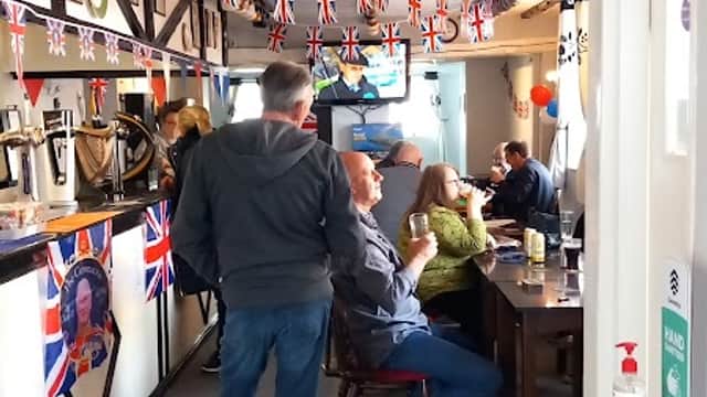 A cozy pub interior decorated with Union Jack flags, featuring patrons enjoying drinks and a TV in the background.