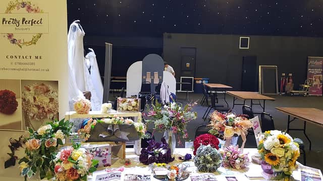 Colorful bouquets displayed on a table with wedding dresses in the background and a promotional banner for Pretty Perfect Bouquets.