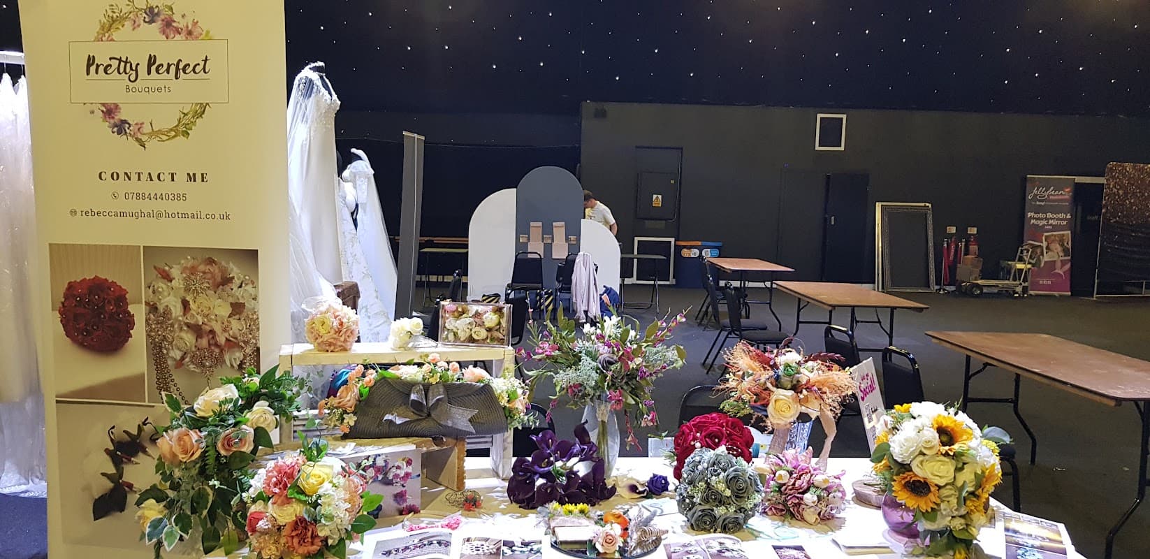 Colorful bouquets displayed on a table with wedding dresses in the background and a promotional banner for Pretty Perfect Bouquets.