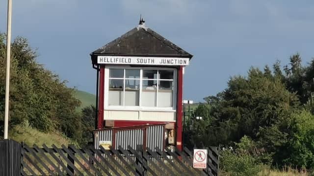 Hellifield South Junction signal box with a black wooden fence and green hills in the background under a clear sky.